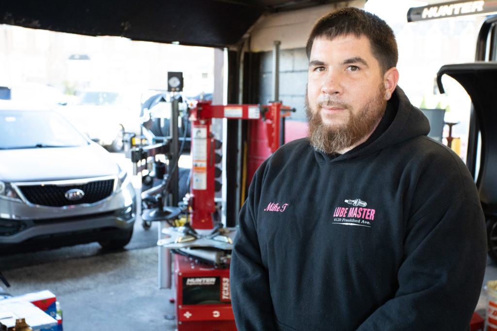 Mike T from Lube Master standing inside a service garage with a line of cars behind him.
