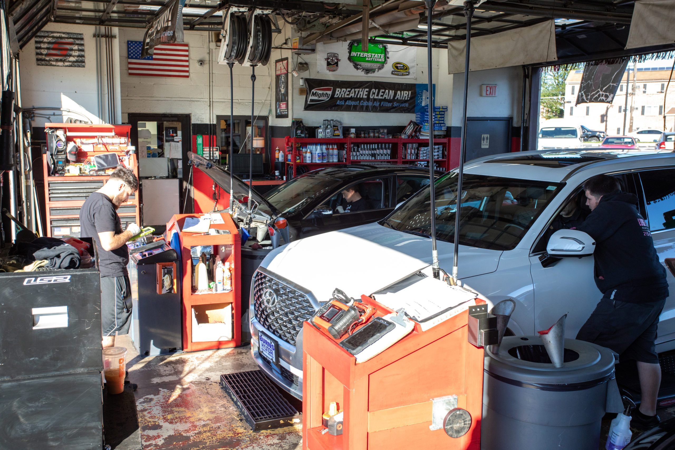 Two cars inside of a service garage being prepared for maintenance by Lube Master employees.
