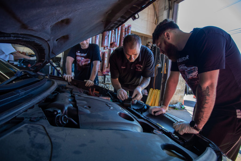 A group of Lube Master employees examines a car’s engine.